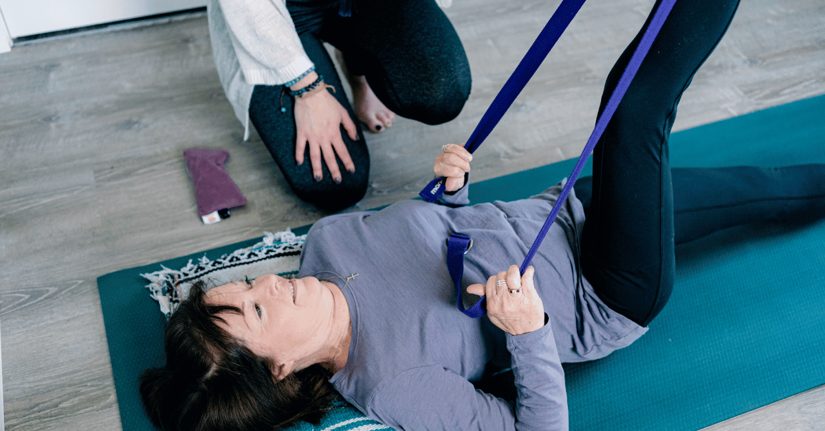 Private yoga therapy session. Yoga therapist and client stretching with yoga strap.