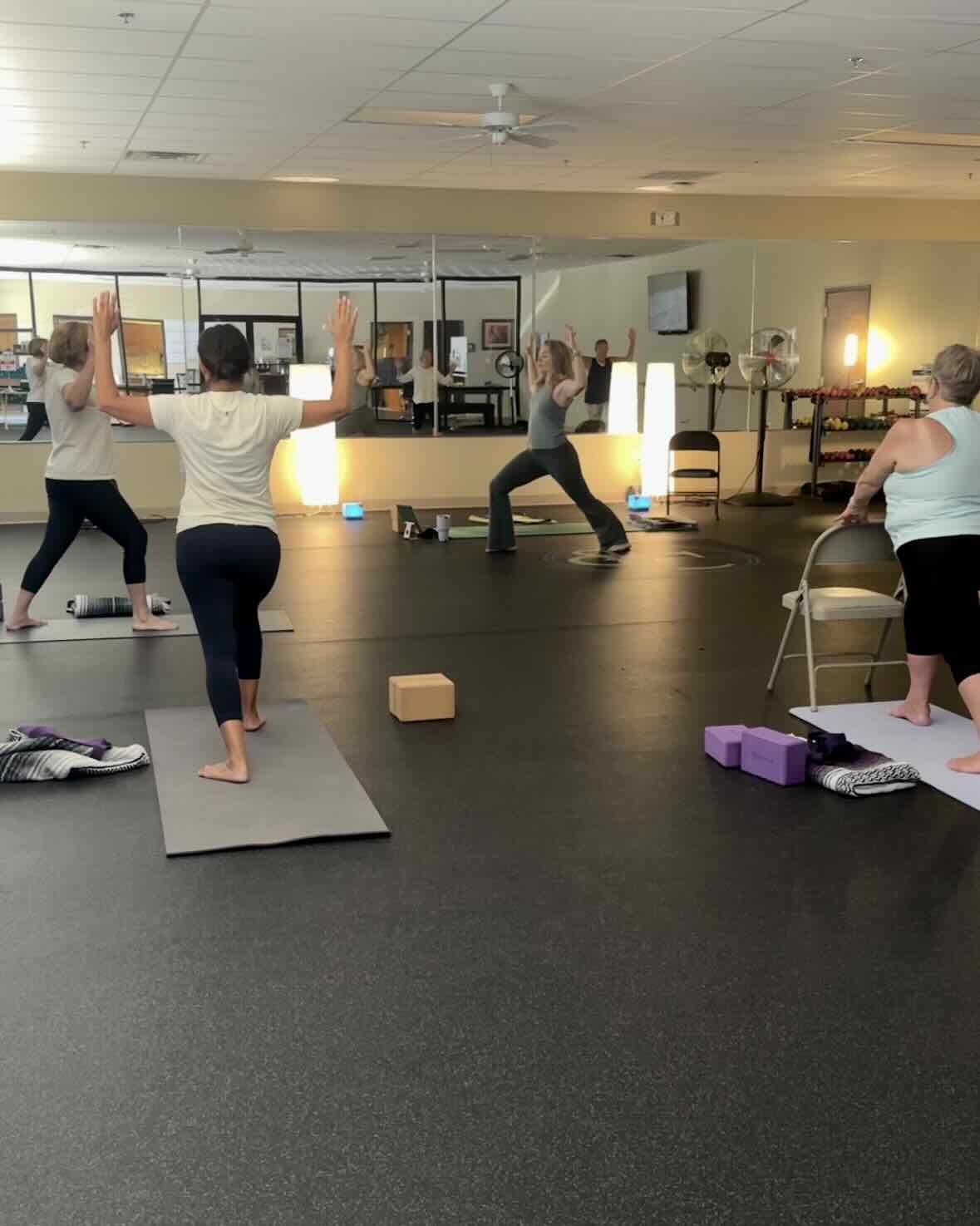 A beginner class of yoga students doing Warrior 1 pose with Mikah Horn teaching the class.