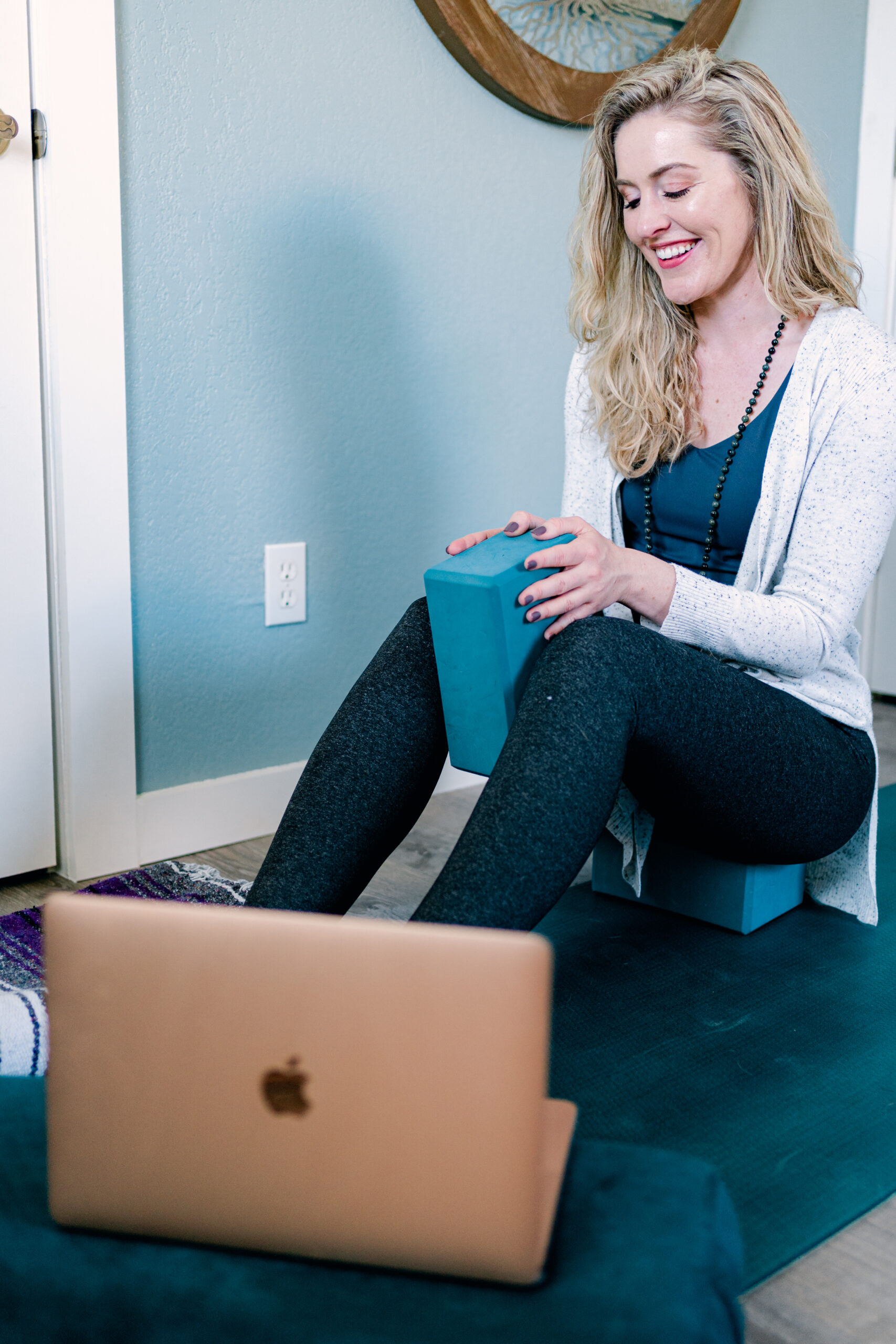 Mikah teaching online yoga therapy with her laptop and a yoga block.