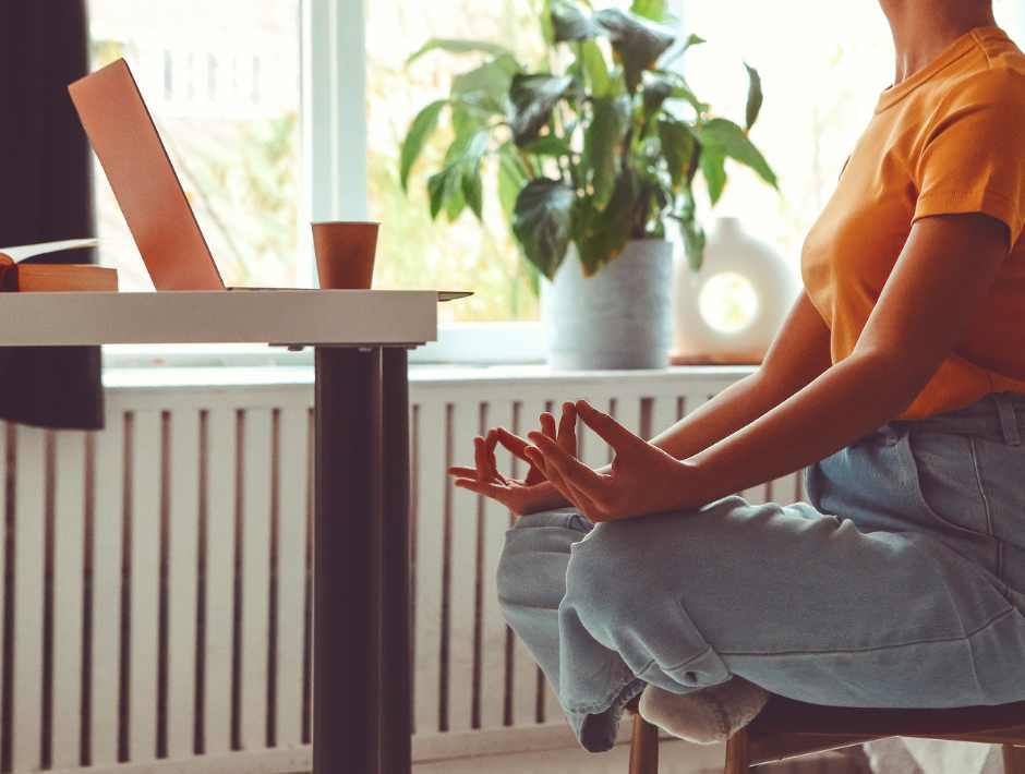 Woman sitting at table doing yoga on her laptop.