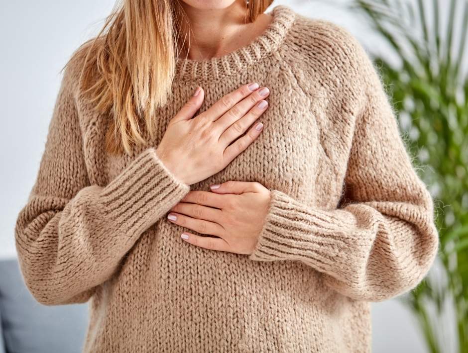 Woman in tan sweater with hands on chest, taking breaths. Yoga for chronic pain