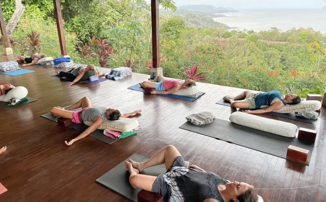 Group at a yoga retreat doing restorative yoga on a deck overlooking the ocean in Montezuma, Costa Rica.